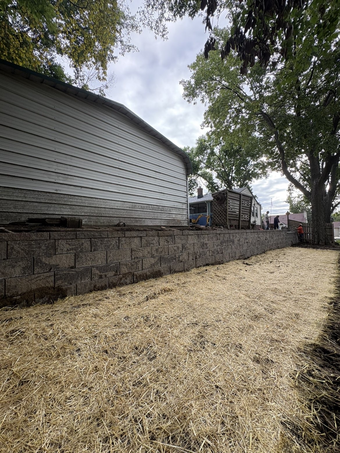 New block retaining wall with fresh straw mulch lawn restoration behind a Des Moines, Iowa home