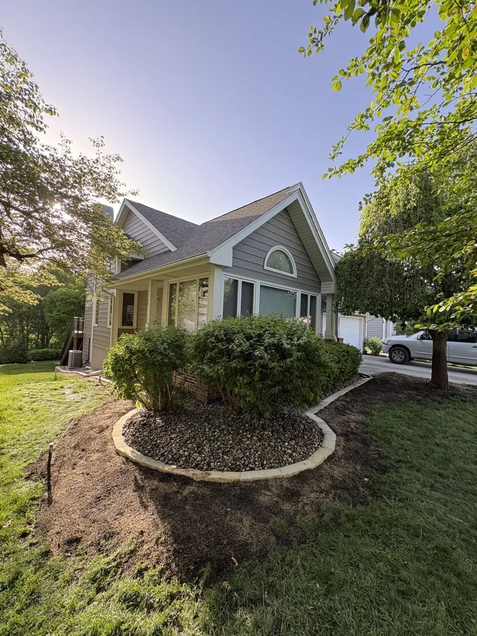 Custom stone landscape curbing with river rock and fresh mulch bed in Des Moines Iowa front yard