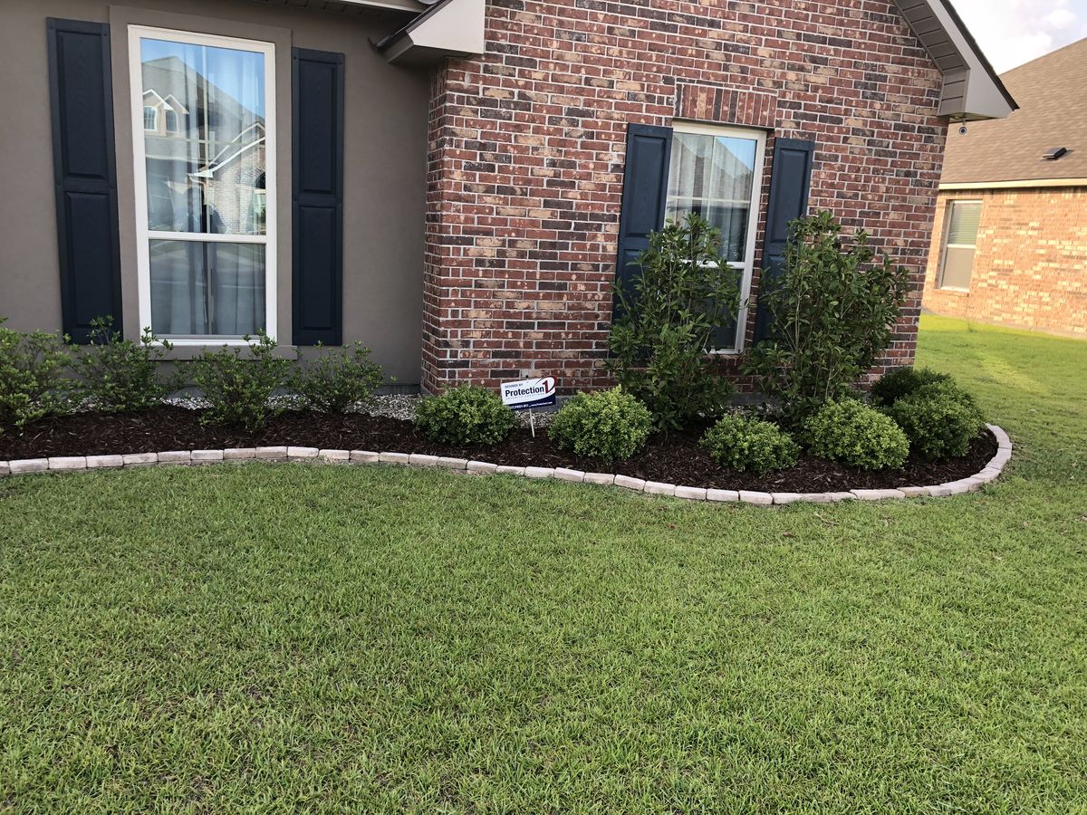 Mulch bed with shrubs and stone border at brick home