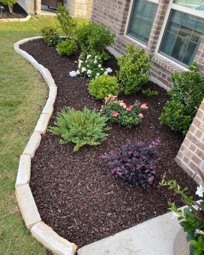Brown mulch flower bed with mixed plantings and stone border