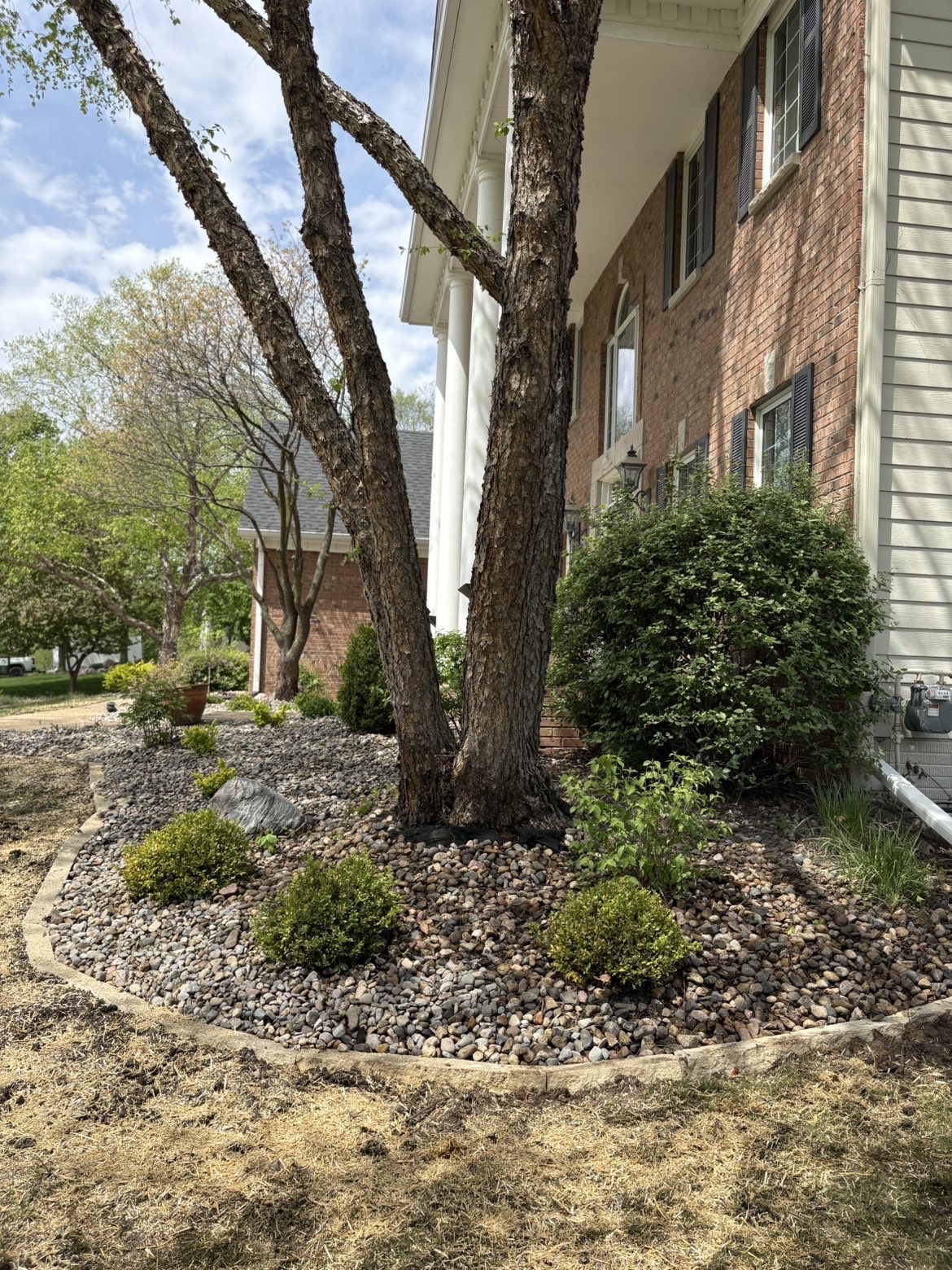 Natural stone landscape edging with river rock bed under tree in Des Moines Iowa