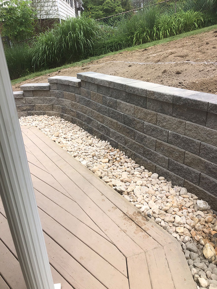 Grey block retaining wall and drainage rock beside a backyard deck in Des Moines, IA