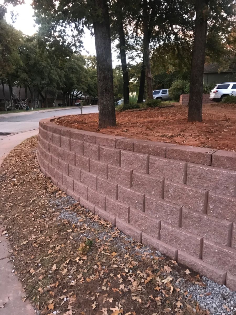 Large red block retaining wall with trees along street in Des Moines